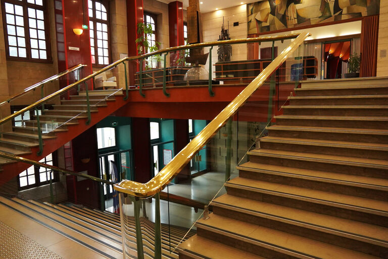 Escalier principal de la Halle aux Toiles avec rampes métalliques dorées, desservant les différents niveaux du bâtiment au sein d’un vaste hall.