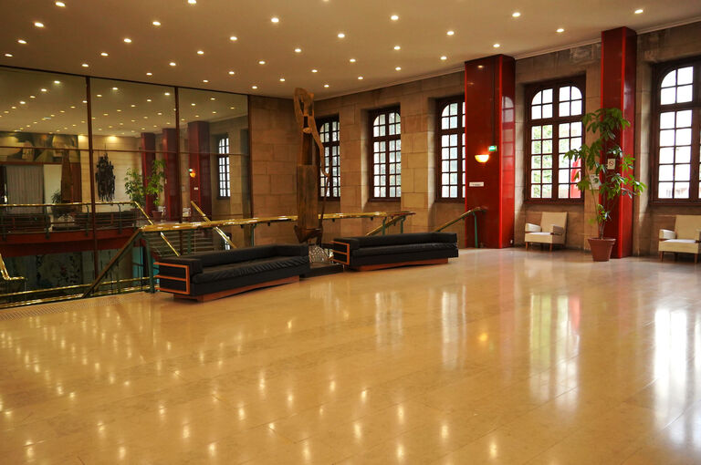 Foyer du premier étage de la Halle aux Toiles avec colonnes rouges, sols clairs.