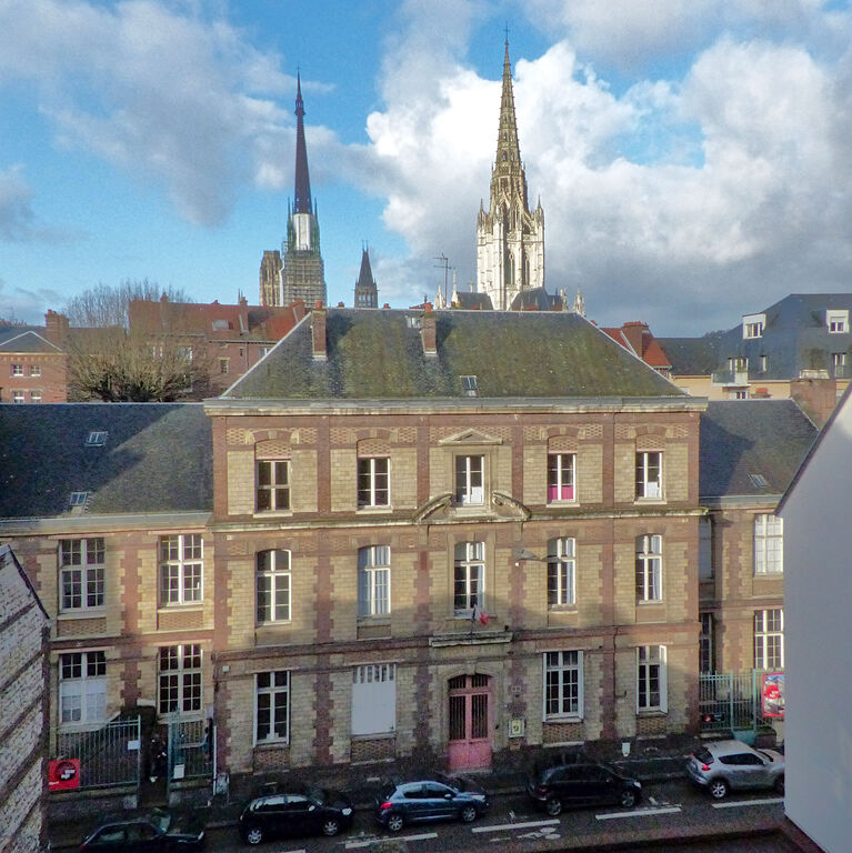 Vue extérieure du bâtiment principal du Labo Victor Hugo, édifice en briques et pierre situé en ville, la cathédrale et l’église Saint-Maclou sont visibles à l’arrière-plan.