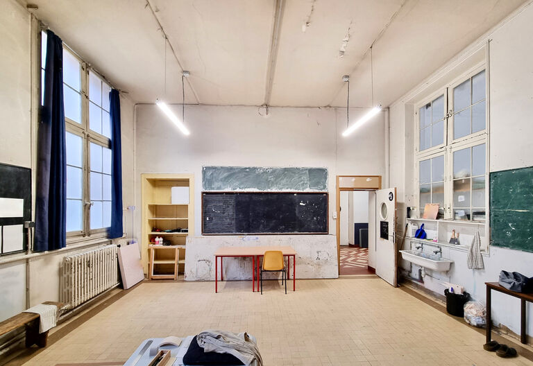 Salle 5 du Labo Victor Hugo avec tableaux noirs, évier, grandes fenêtres et mobilier simple, offrant un vaste espace de travail pour les artistes.