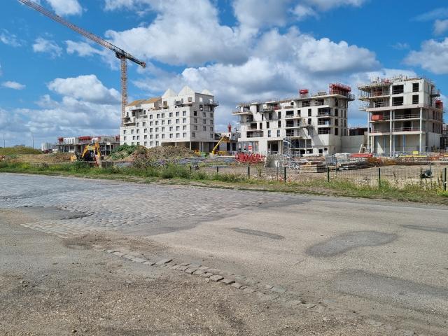 Construction de deux immeubles gris sur fond de ciel bleu et devant une large zone bitumée