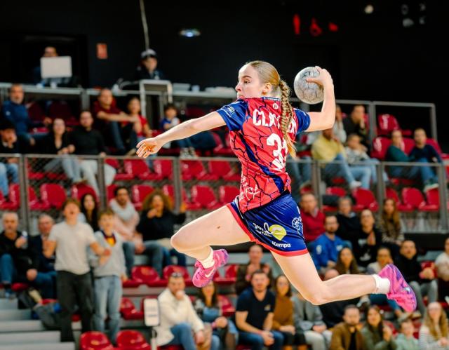 Match de handball Rouen-Rennes Une joueuse du Rouen Handball en short bleu et maillot rouge fait un tir en extension avec le ballon dans la main gauche