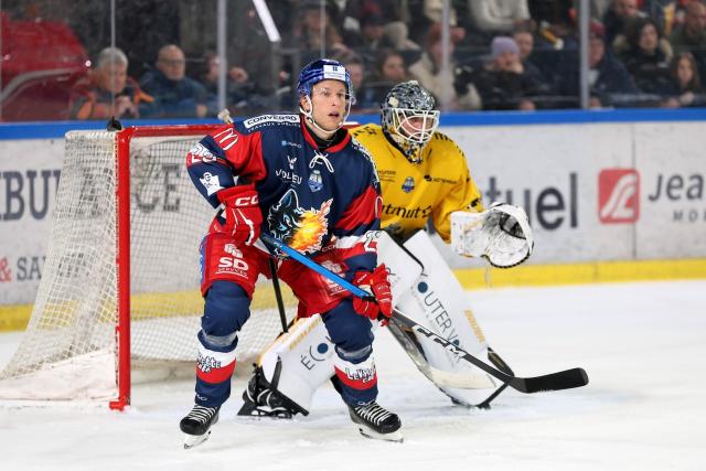 L'attaquant suédois Fredric Weigel en maillot rouge et bleu de Grenoble se tient avec la crosse au sol devant le gardien américain Mac Carruth en maillot jaune de Rouen qui est dans sa cage