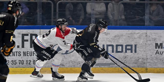 un joueur de Rouen de profil sur la glace tient le palet dans sa crosse et est poursuivi par un joueur de Bordeaux en blanc et rouge