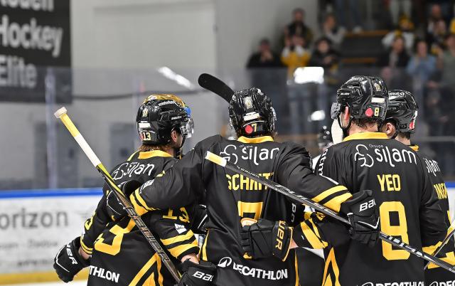 trois joueurs de Rouen en maillot noir et jauen sont de dos et se congratulent après avoir gagné le match 