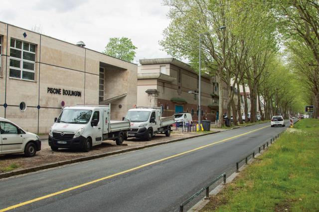 Photo de la piscine Boulingrin vue du boulevard de Verdun avec sa façade beige et devant des camionnettes blanches qui stationnent sur le trottoir 