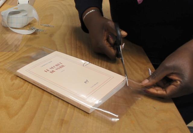 Une personne équipée de ciseaux couvre un livre avec du plastique