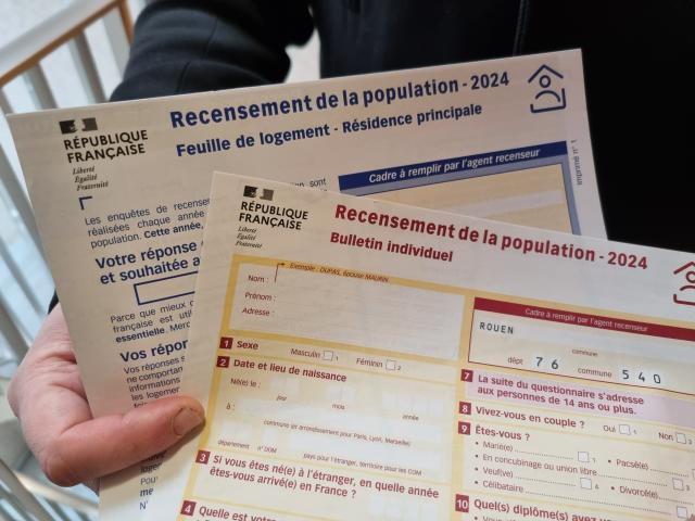 Une main tient les deux questionnaires papier à remplir par les habitants recensés